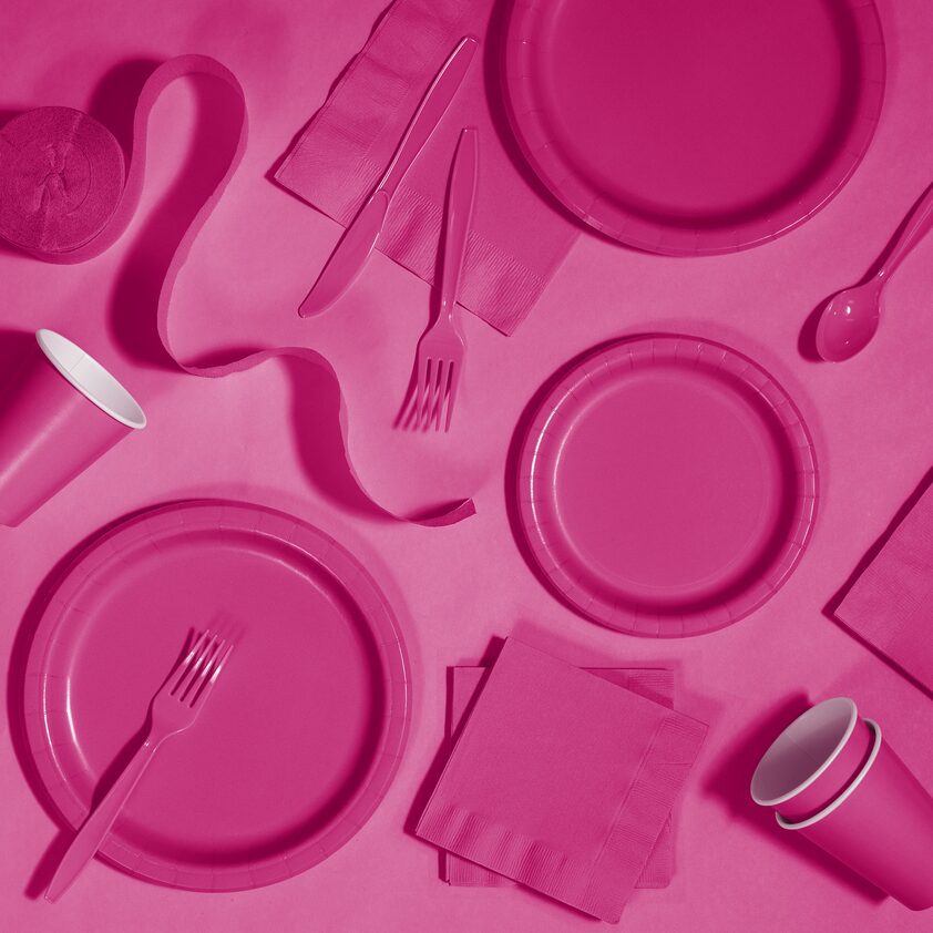 A pink table cloth with plates, cups and napkins.